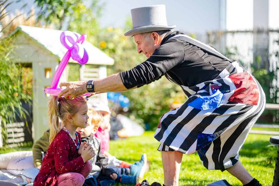 Kinderzauberer und Ballonkünstler Michael setzt einen lächelnden Mädchen eine Ballonkrone auf den Kopf